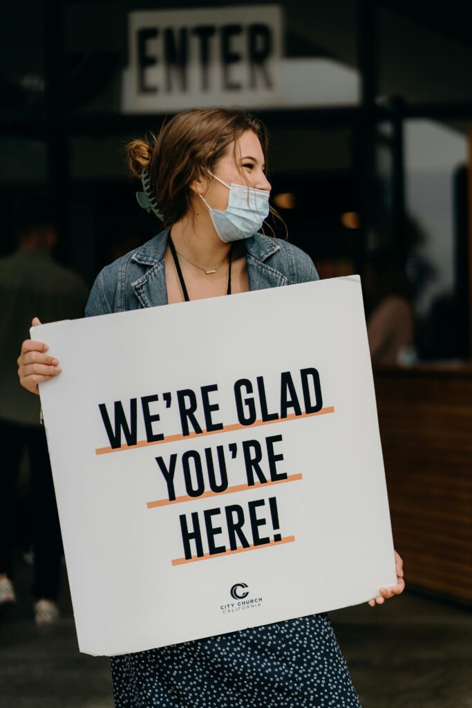Woman welcoming people with sign that says, "We're glad you're here!"